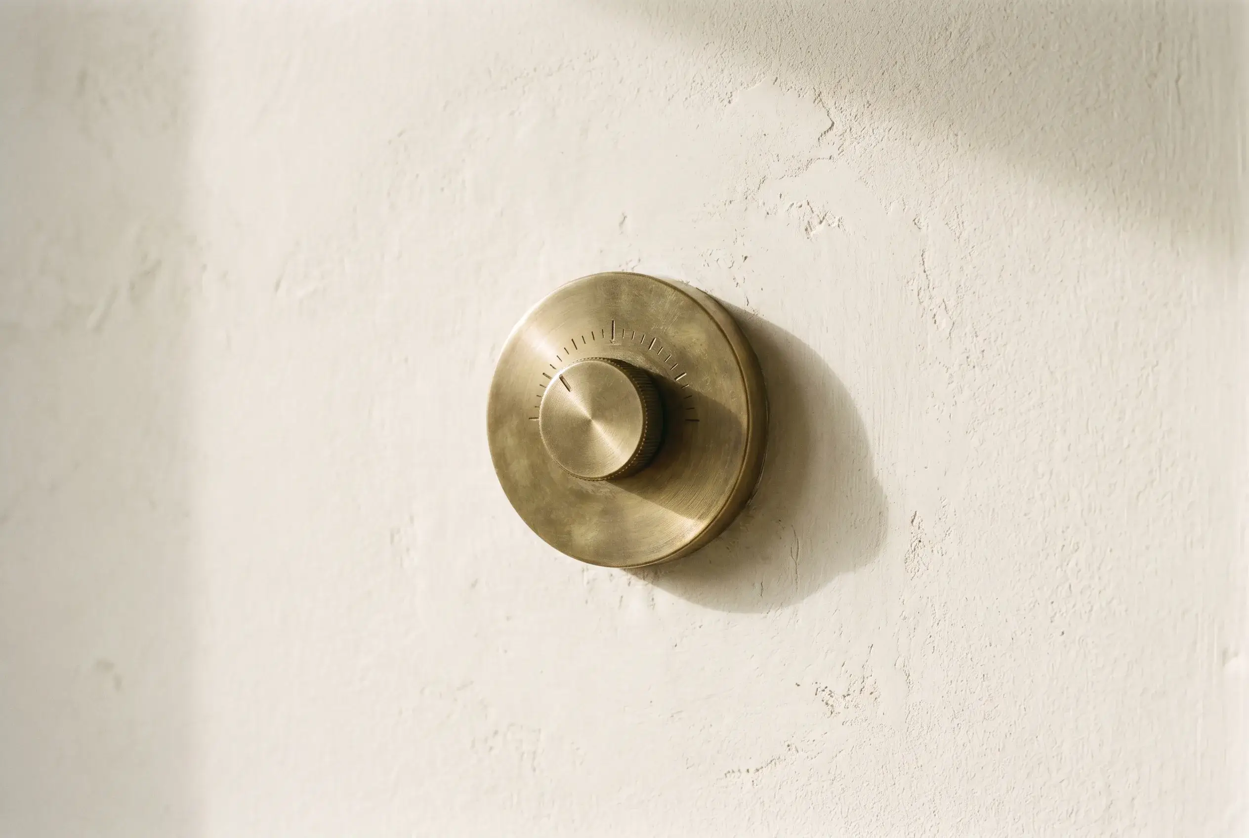 A solid brass rotary dimmer set into a plaster wall