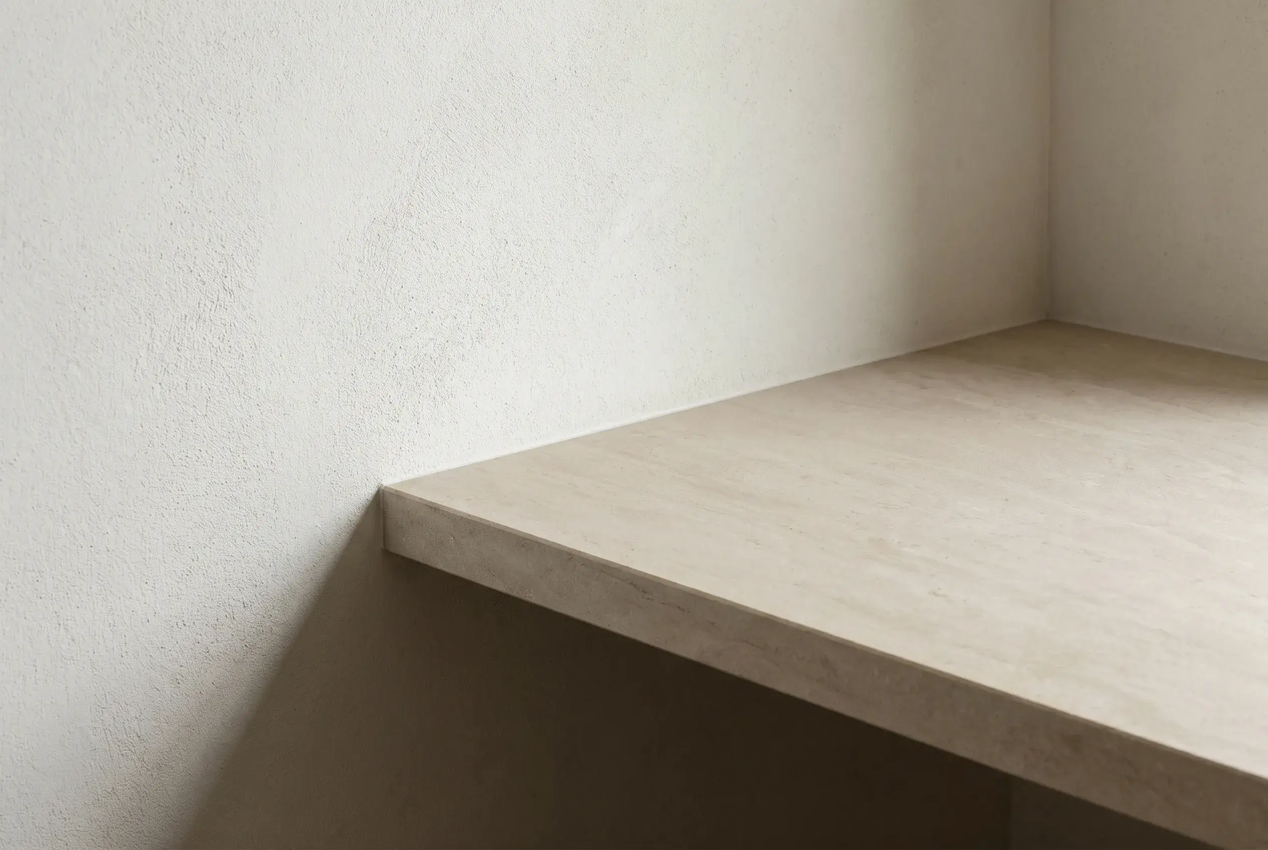 A travertine shelf set into a hand-trowelled plaster wall